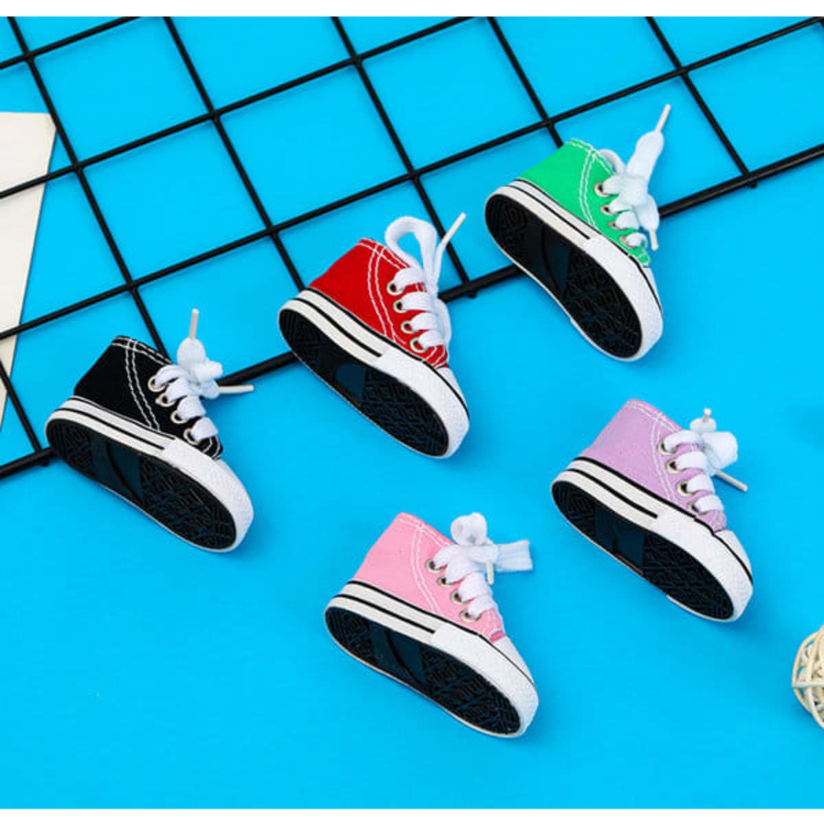 A collection of mini canvas sneaker keychains in black, green, red, pink, and purple, displayed on a blue background.