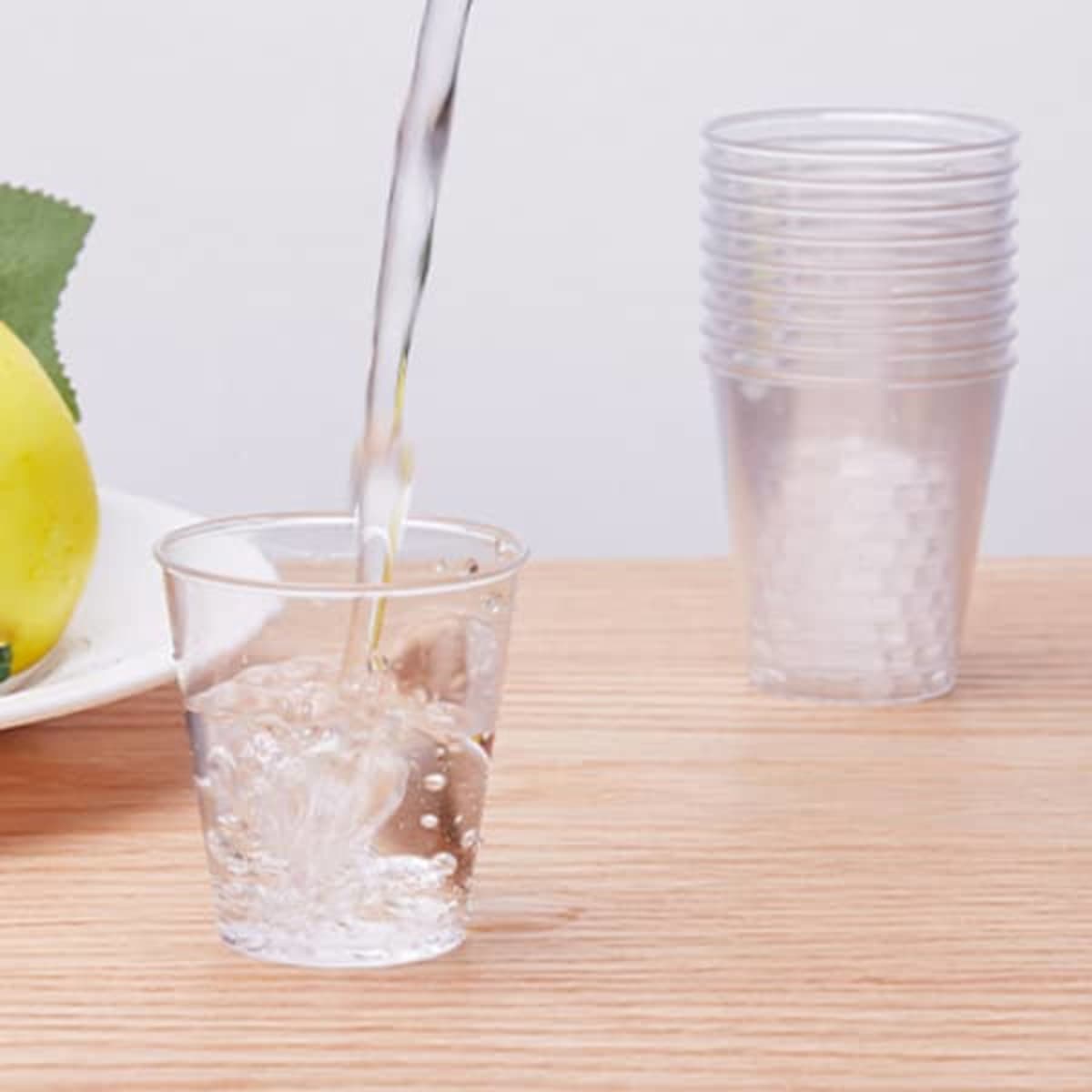 A clear plastic party cup being filled with liquid, with stacked cups visible in the background.
