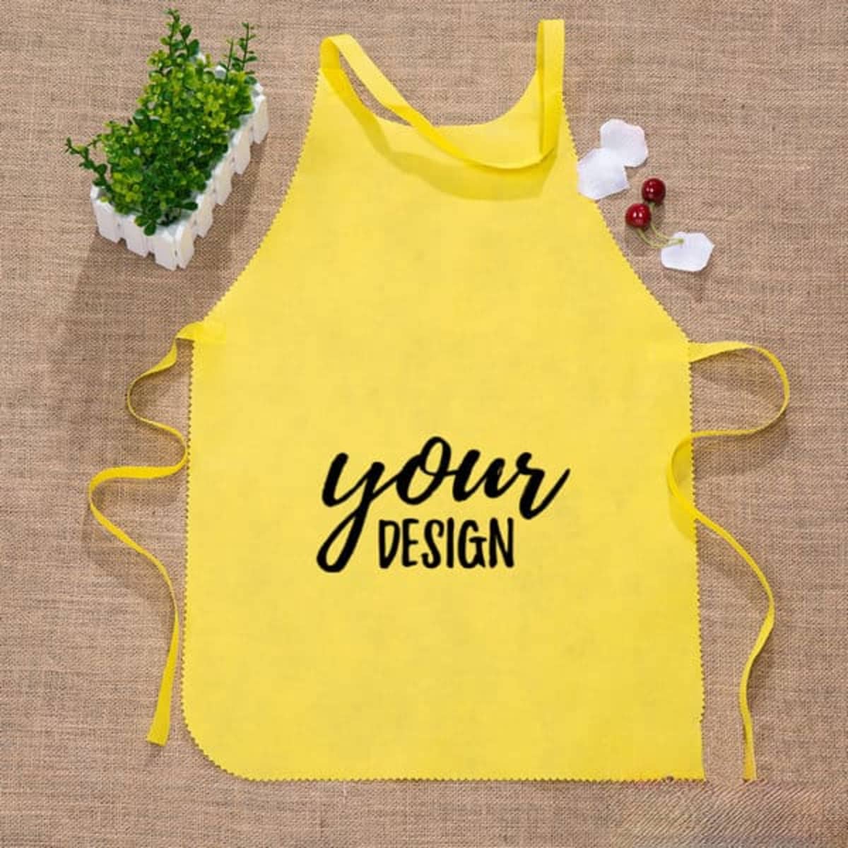 A yellow waist apron with ties, featuring a space for custom design and a logo. Green plant and decorative elements nearby.