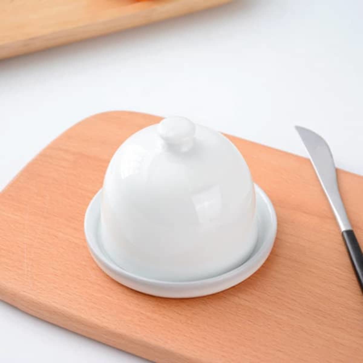 A white porcelain cake stand with a dome, placed on a wooden surface alongside a knife.