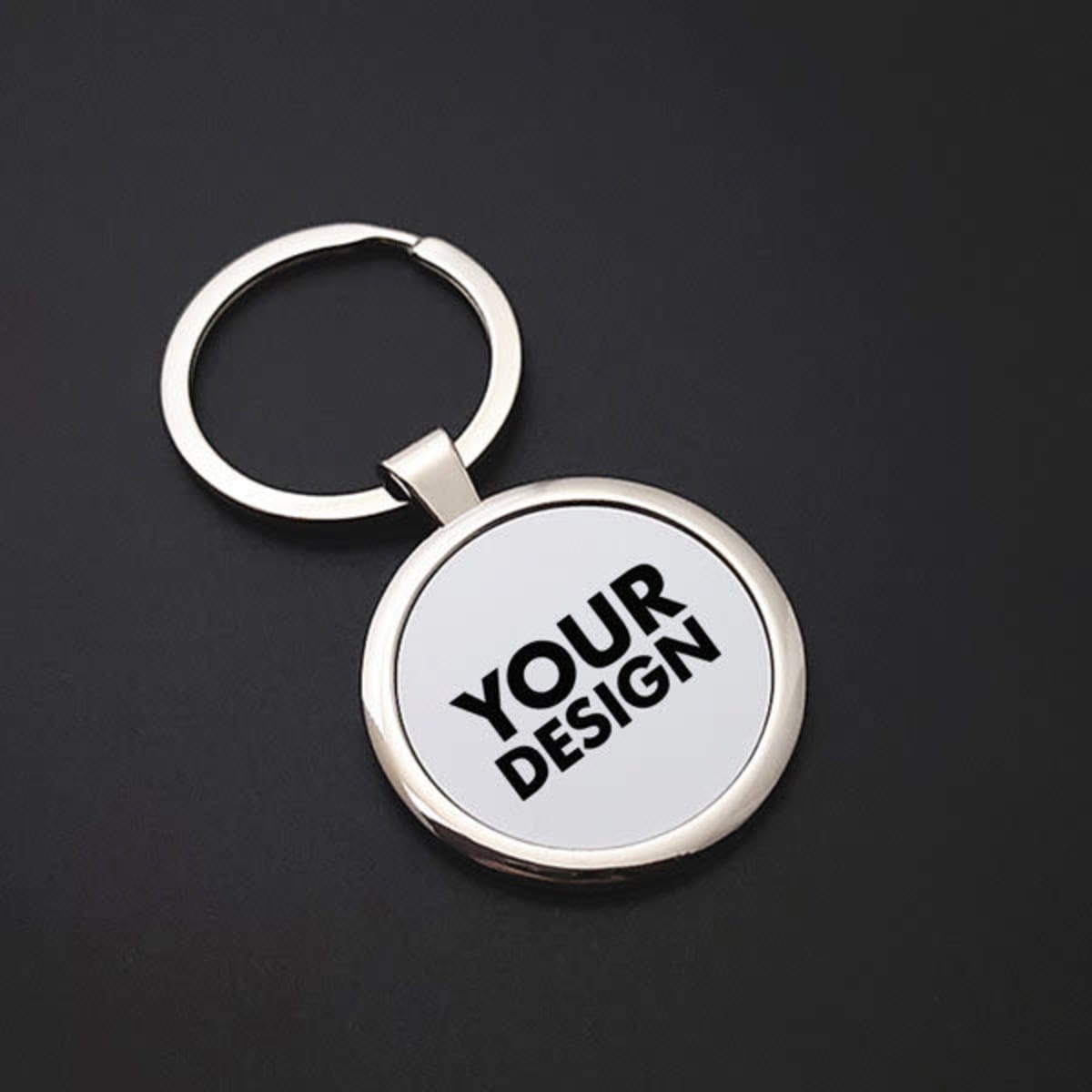 A silver metal keychain with a circular blank space for personalisation, set against a dark background.