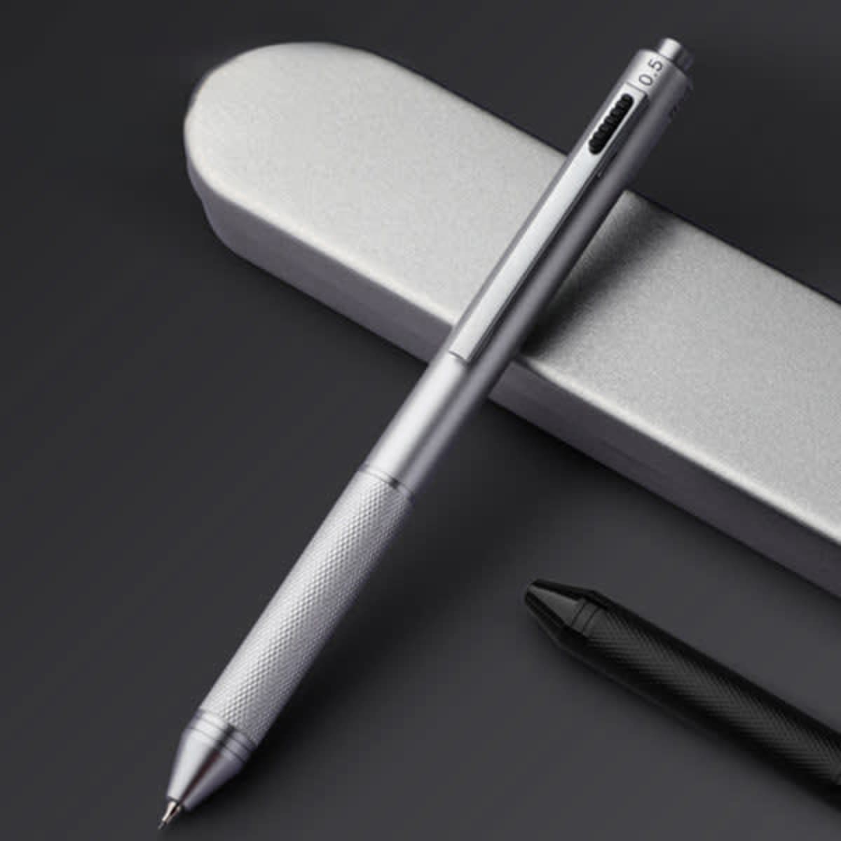 A silver 4-in-1 ballpoint pen sits atop a sleek grey case, featuring a textured grip and a black pen nearby.