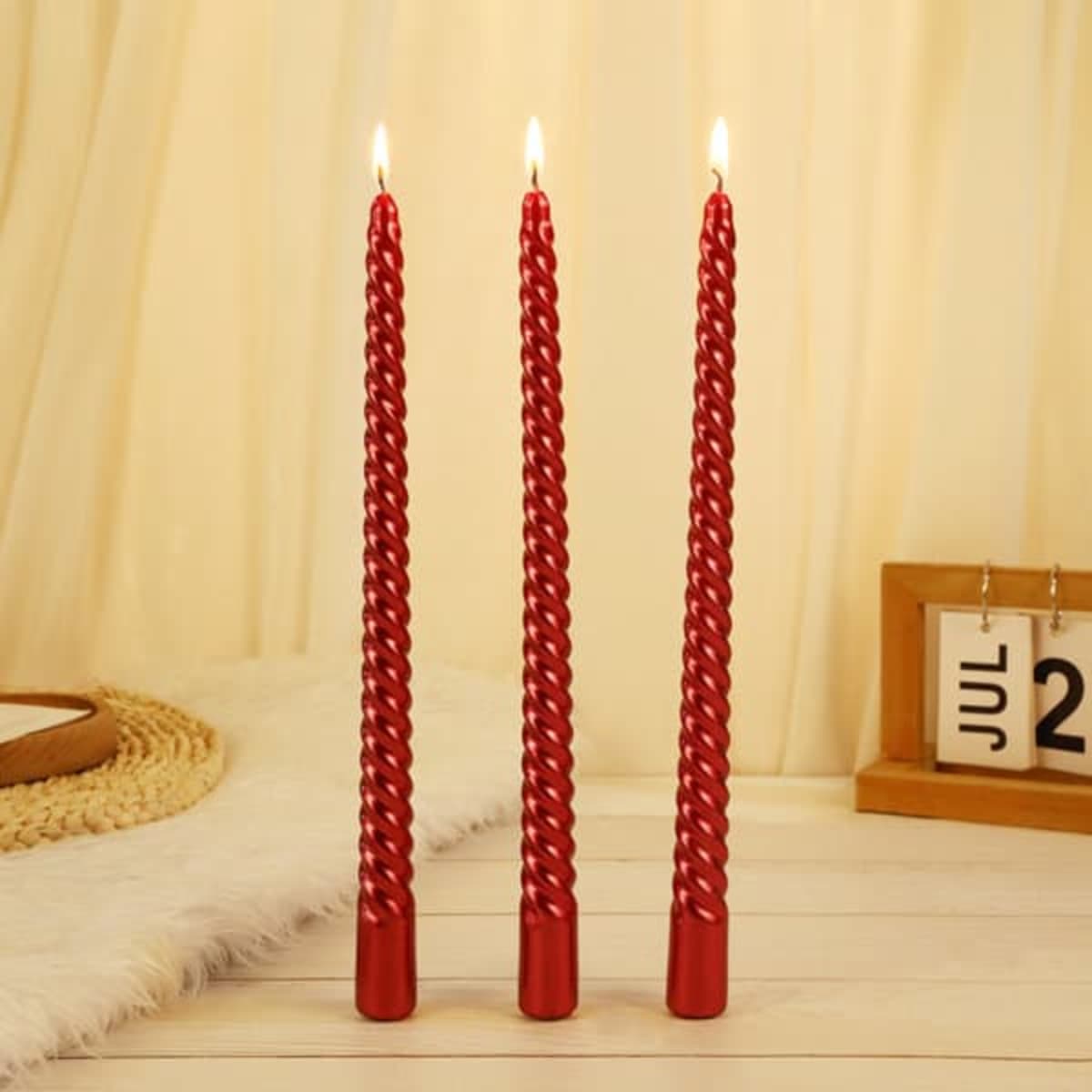 A set of three red spiral taper candles, each lit, displayed against a soft background.