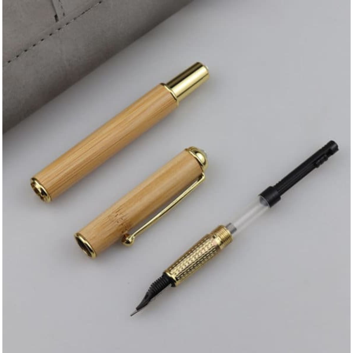 A Natural Bamboo Fountain Pen Gift Set featuring a bamboo pen and a gold-accented pen cap on a grey background.