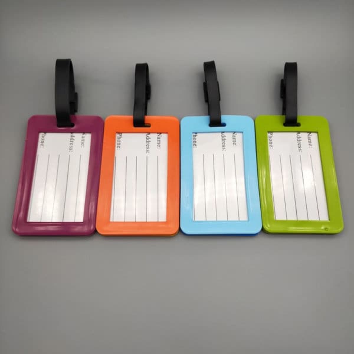Four luggage tags in purple, orange, blue, and green, each featuring a name ID card area and a black strap.