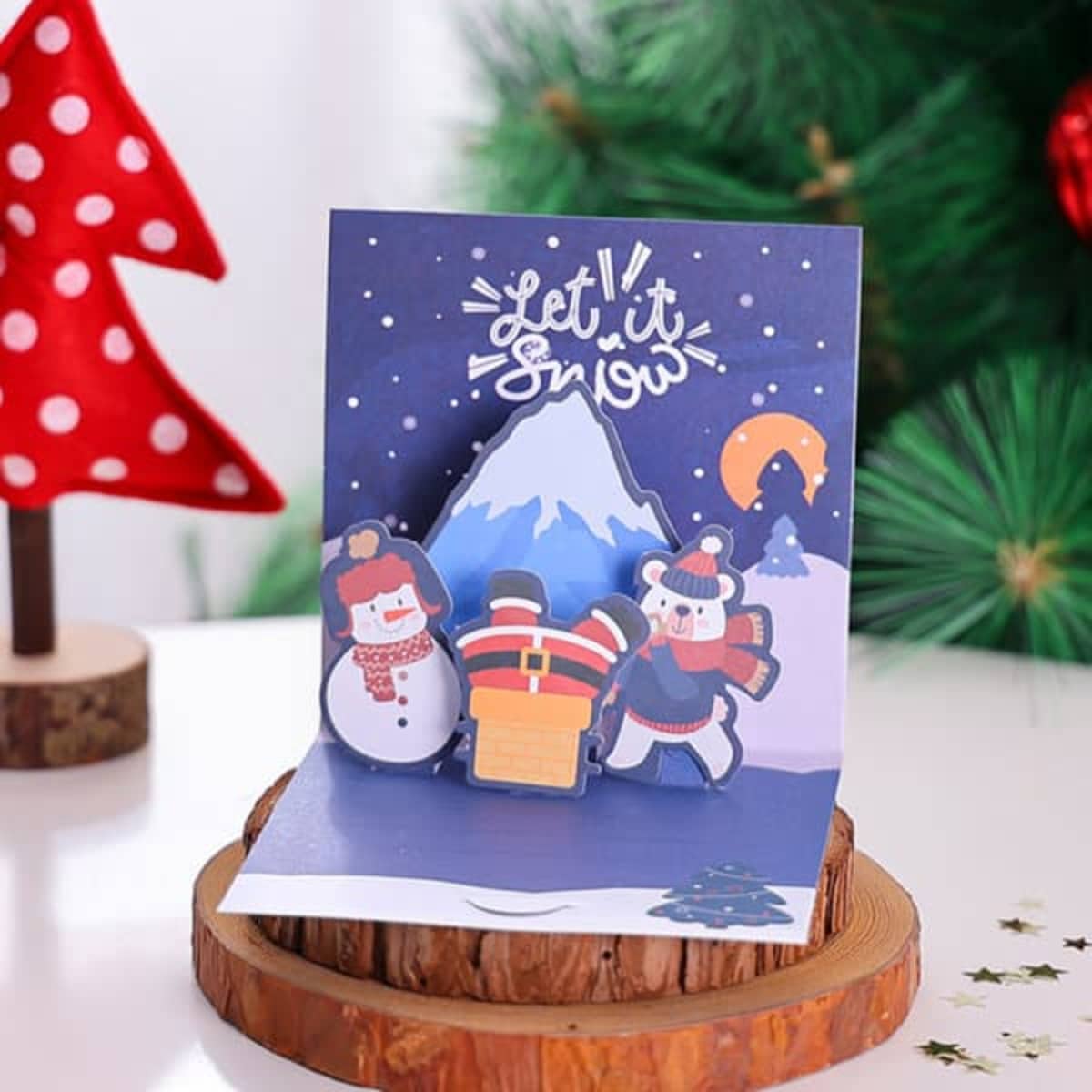 A 3D pop-up greeting card featuring snowmen, a mountain, and festive colours against a winter scene backdrop.