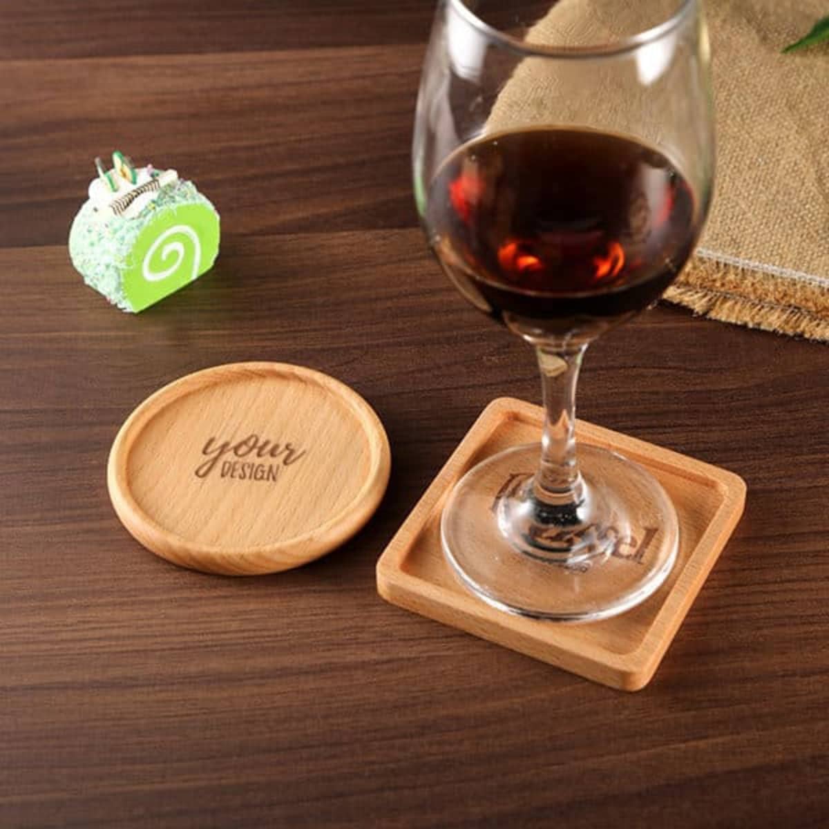 A wooden drink coaster with a square shape beside a round coaster. A wine glass sits on the square coaster.
