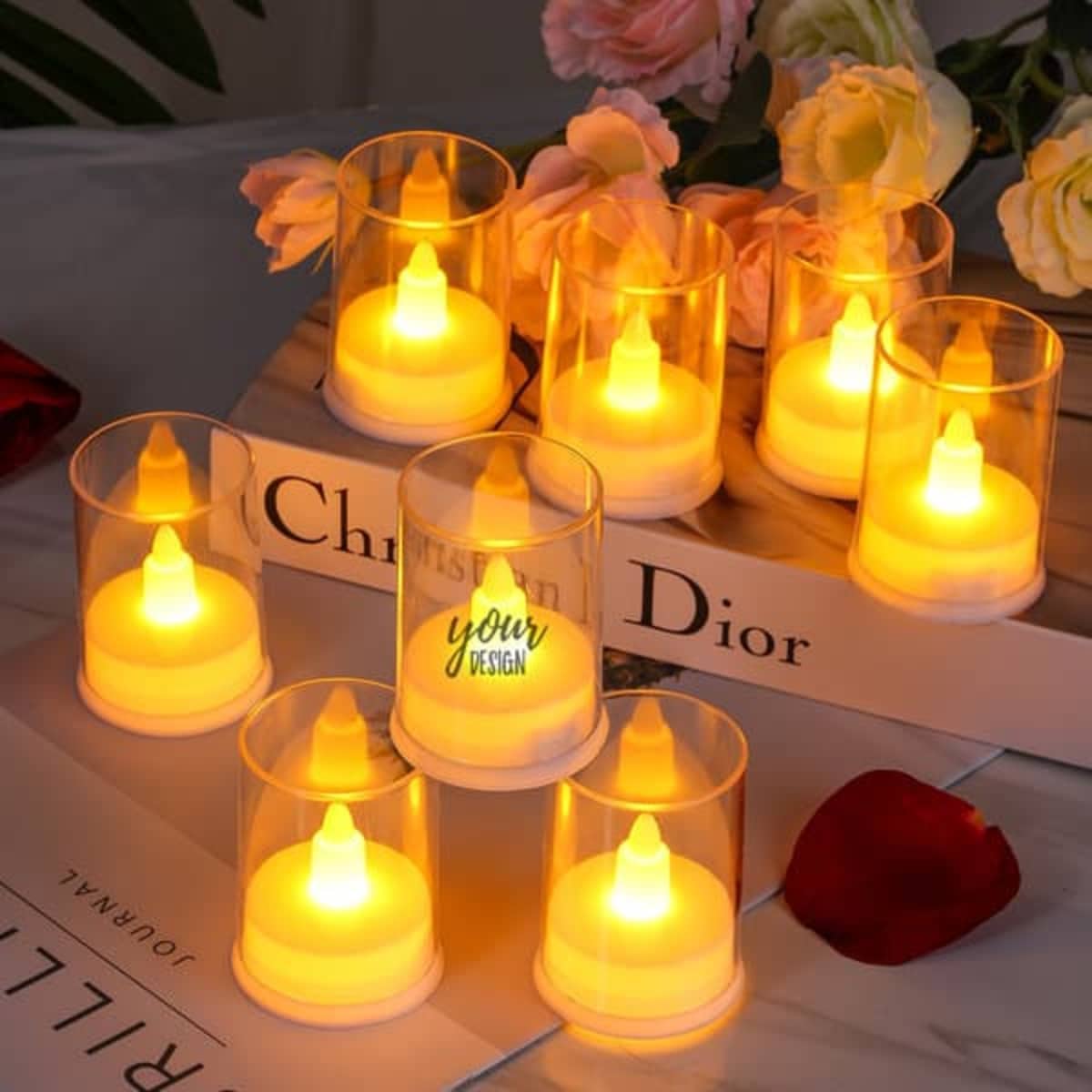 A set of flameless candles in glass holders, featuring a warm yellow glow, arranged with flowers and books.
