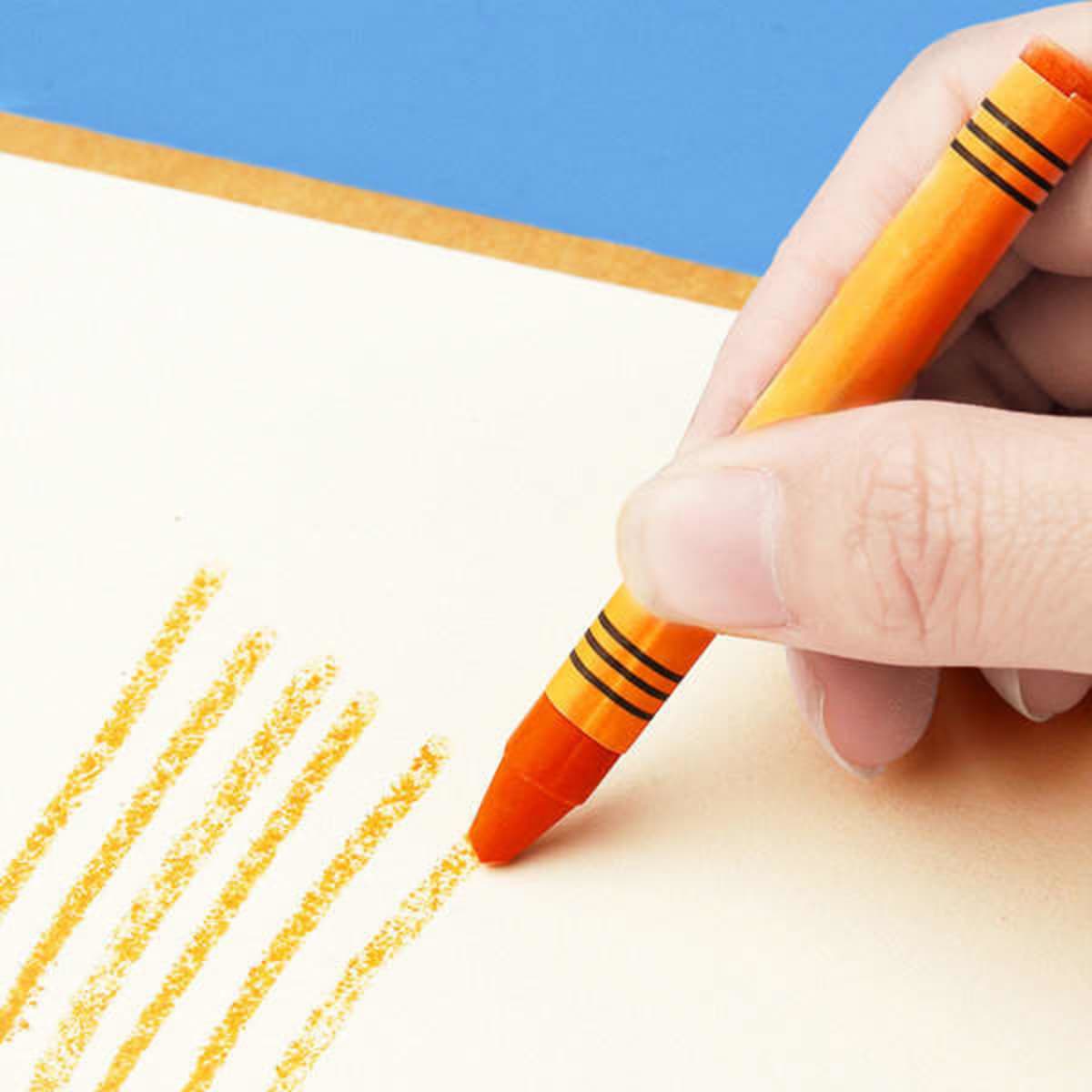 An orange crayon being used to draw on light-coloured paper. The crayon has black stripes and is part of a larger set.