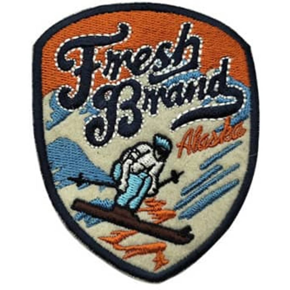 A custom embroidery patch featuring a snowy mountain scene with a skier, predominantly in blue, orange, and beige.