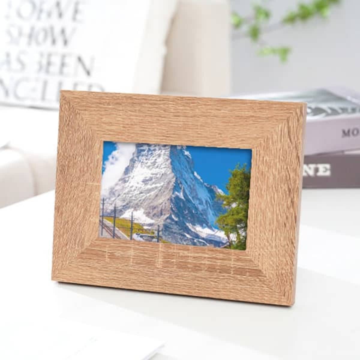 A wooden picture frame in a light tan colour, displaying a scenic mountain photograph.