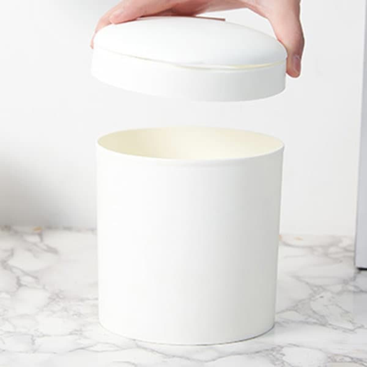 A white mini desktop trash can with a removable lid, sitting on a marble surface.