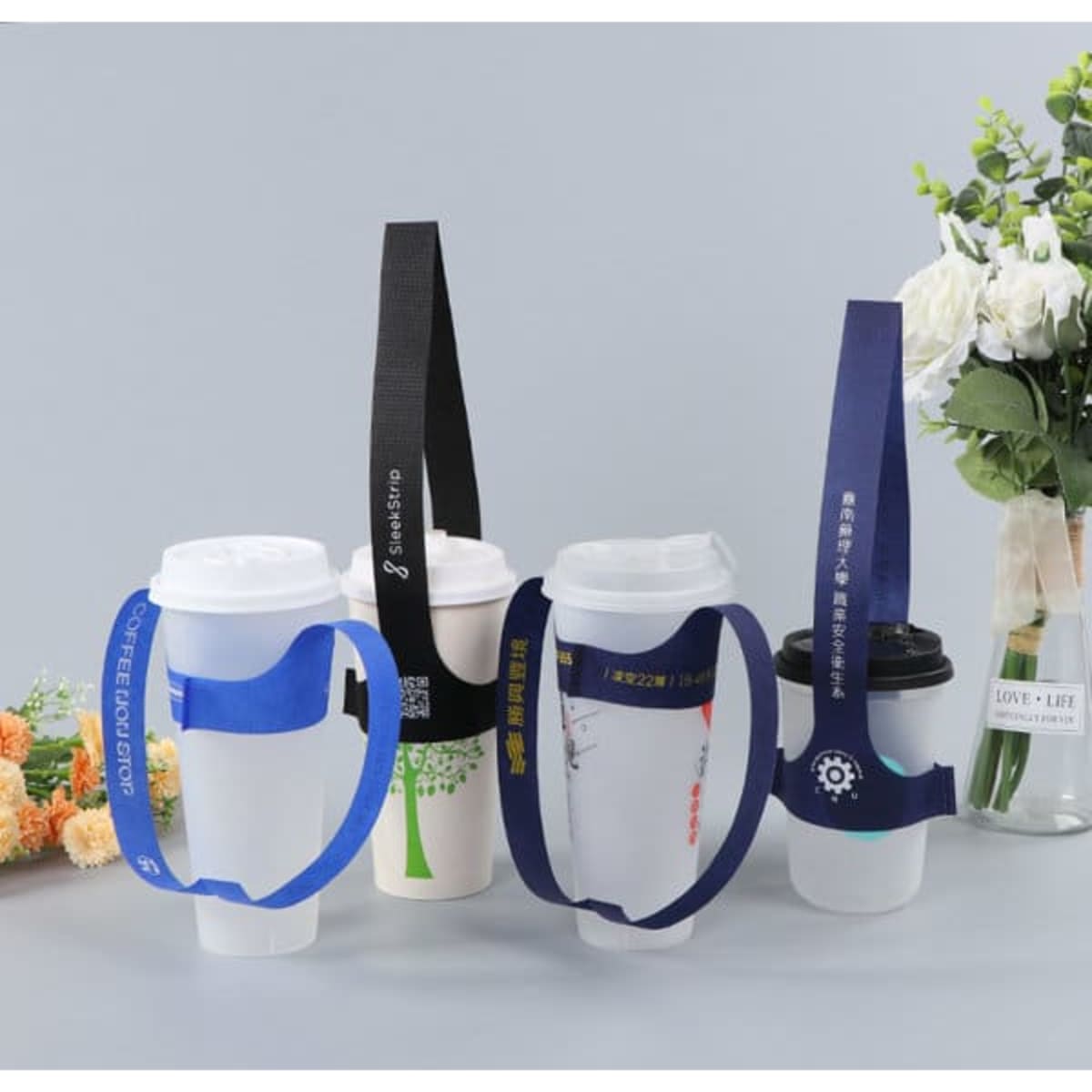 A set of four disposable T-type handle cup carriers in blue and black, with varying strap designs, alongside a floral arrangement.