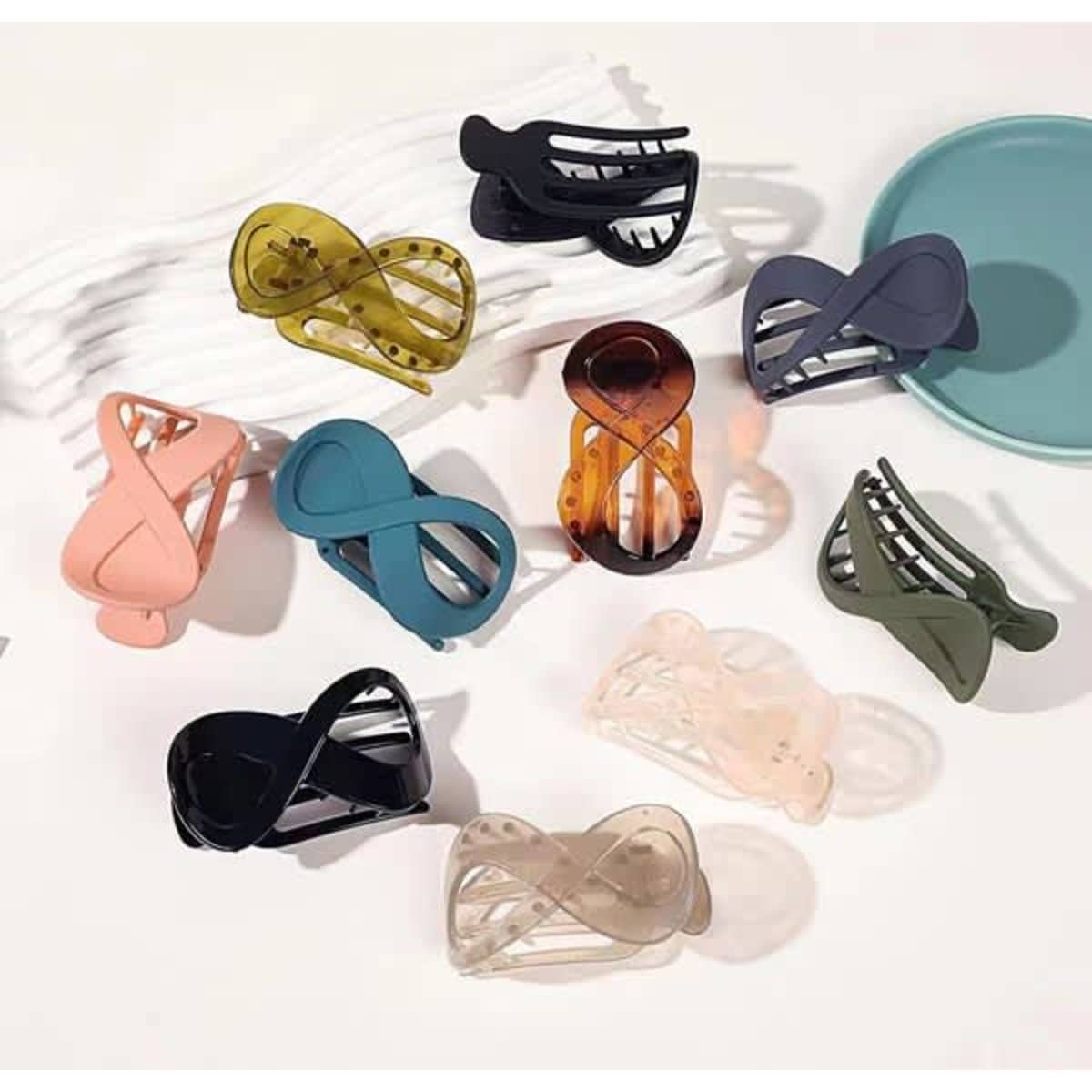 A collection of ten custom hair clips in various colours, including black, peach, green, and transparent, arranged on a surface.