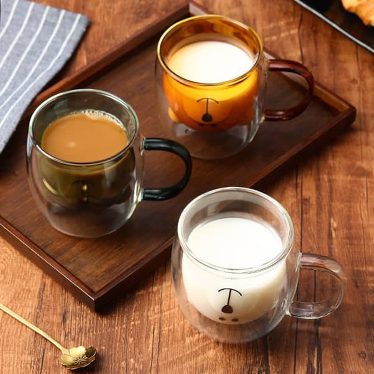 A set of three double wall glass coffee cups in various colours, featuring a black handle and a logo.