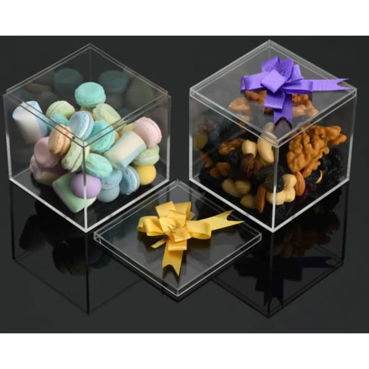 Three transparent acrylic square boxes, each containing colourful sweets, nuts, and a decorative ribbon on top.