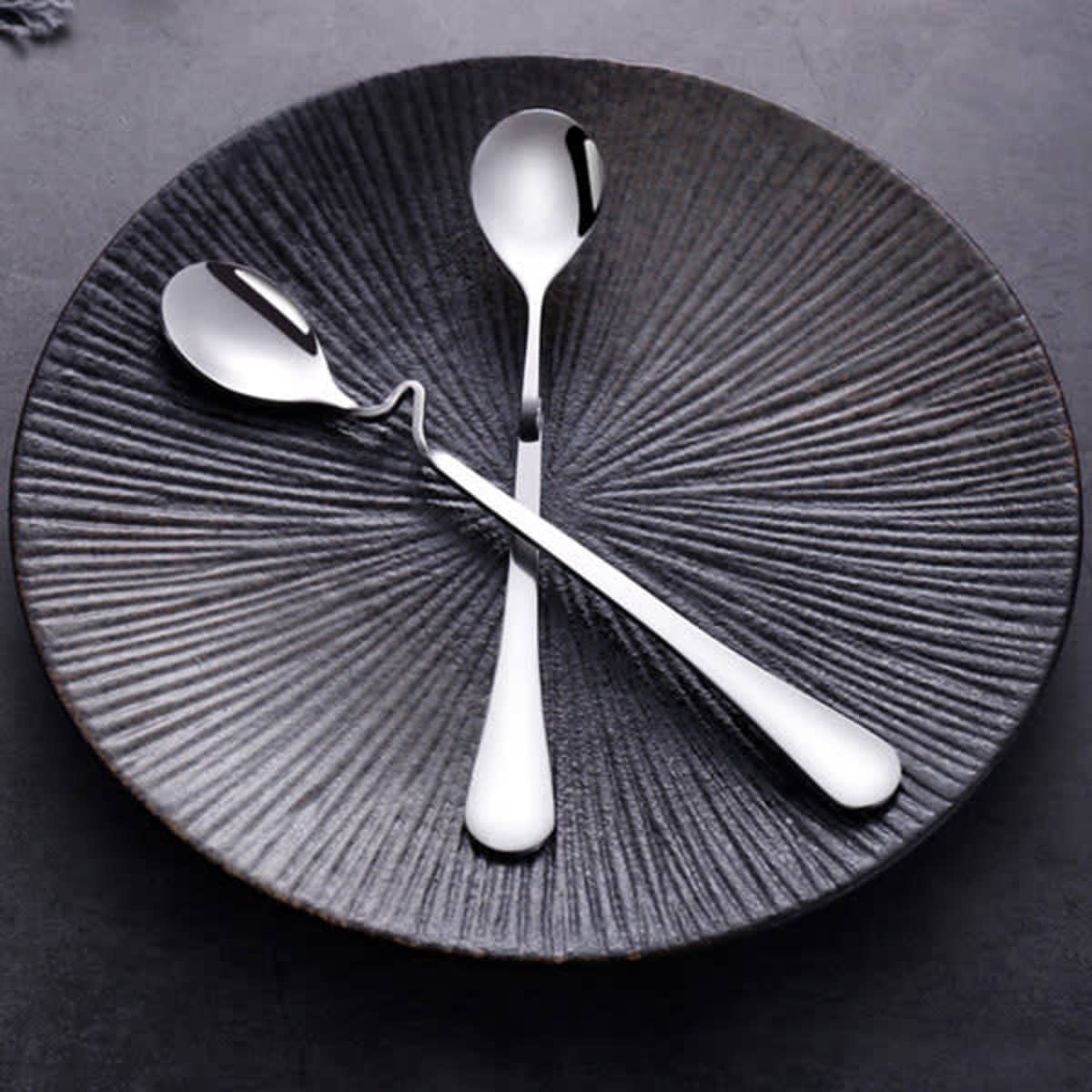 A black plate holds two stainless steel latte spoons with a sleek design, showcasing a shiny finish and elegant curves.