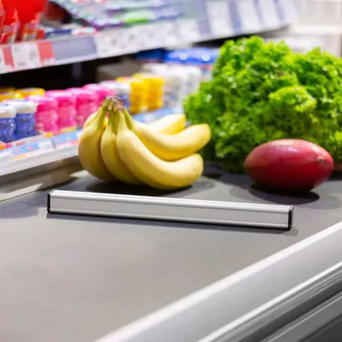 A checkout lane divider in silver, placed alongside bananas and a red apple on a grocery counter, with lettuce nearby.