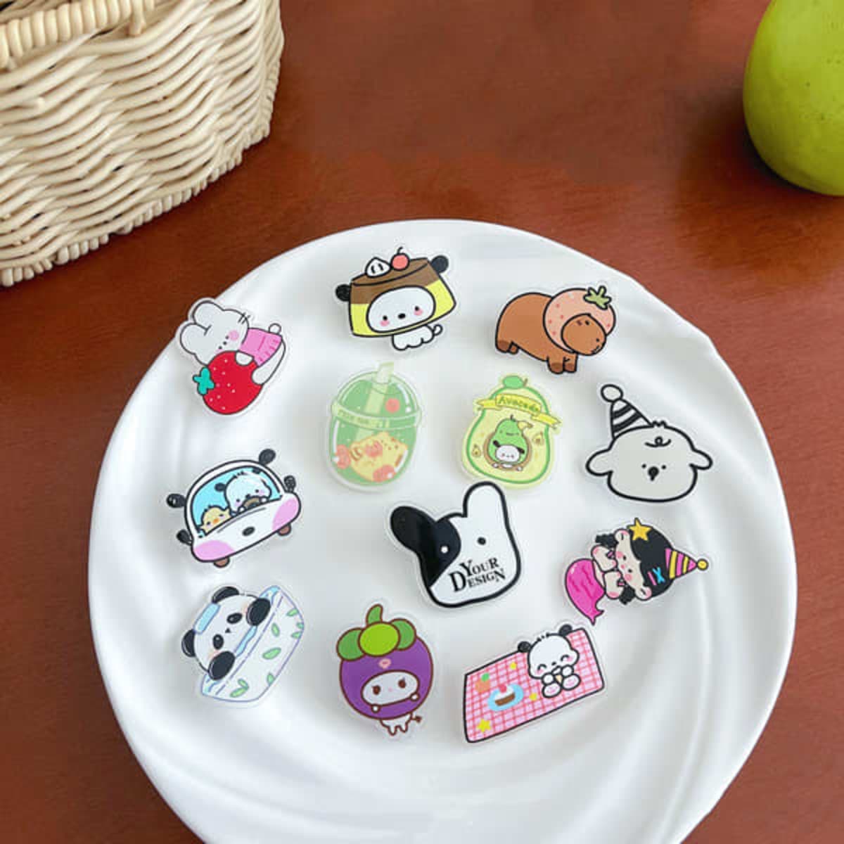 A plate displays various custom acrylic lapel pins in bright colours, featuring cute cartoon designs and a logo.