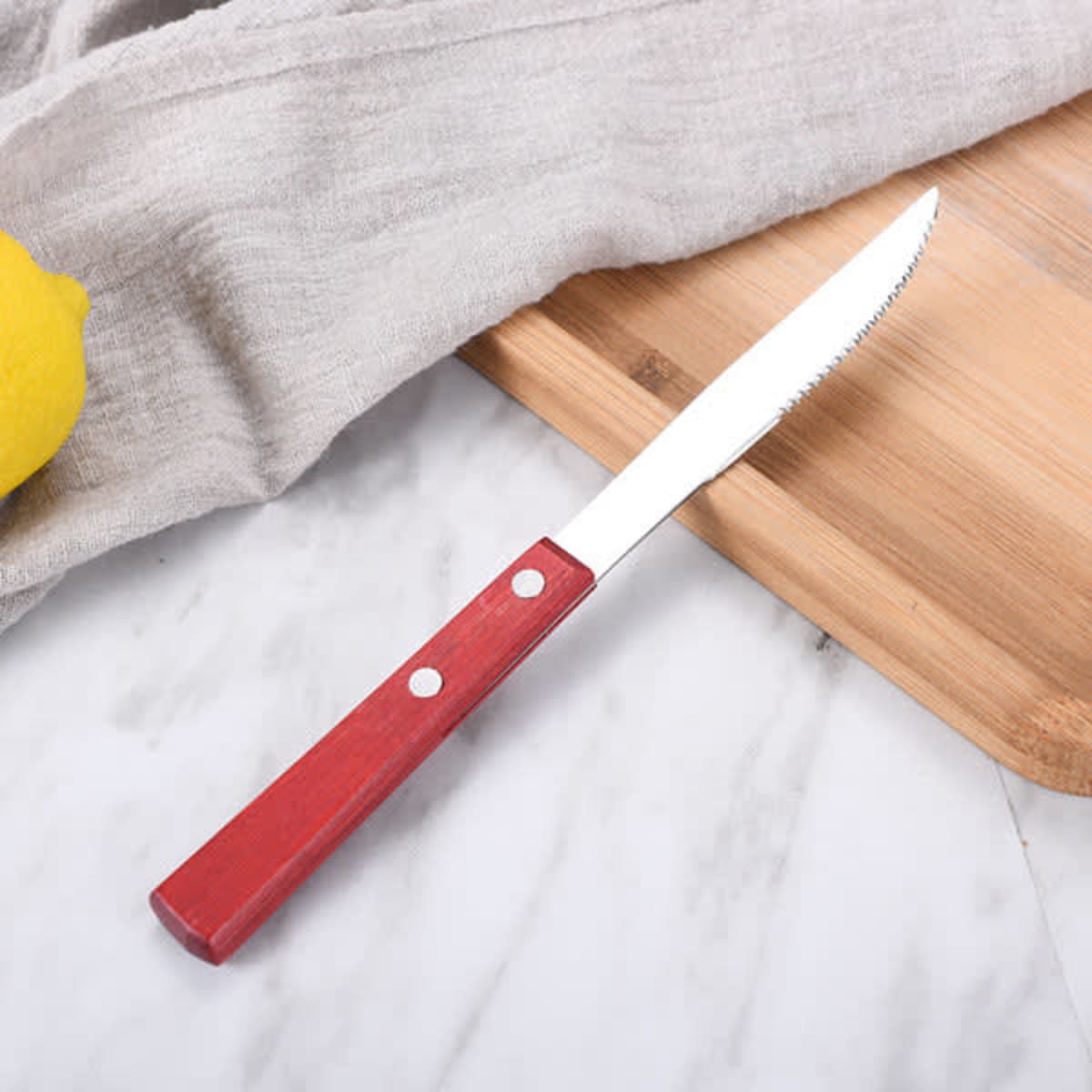 A steak knife with a red wooden handle rests on a cutting board, accompanied by a grey cloth and a lemon.