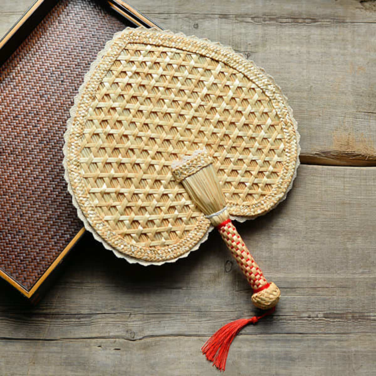A heart-shaped woven fan made of natural wheat straw, featuring a decorative handle with red accents.