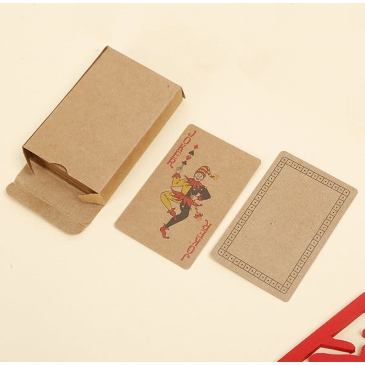 A pack of kraft paper playing cards with a jester design, displayed alongside its kraft paper box.