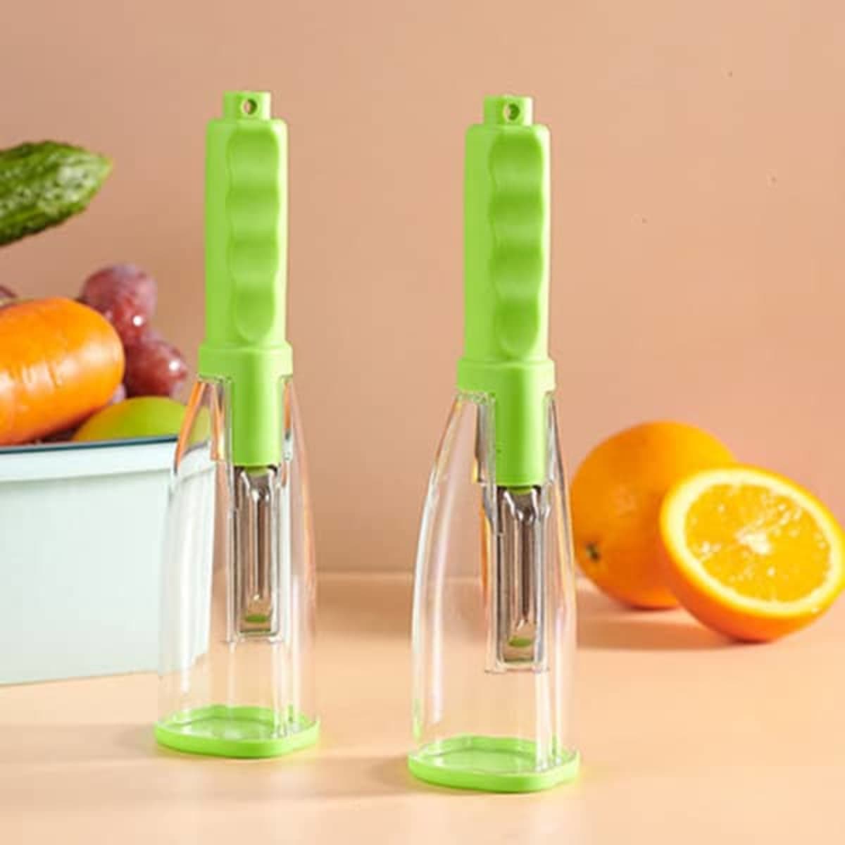 A pair of green peelers with transparent storage boxes, placed against a light background with fruits and vegetables.