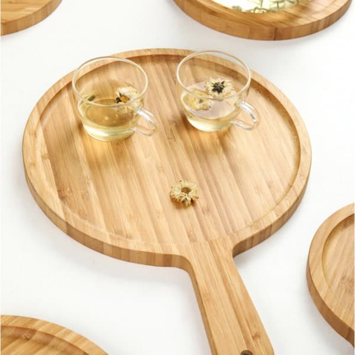 A round solid bamboo pizza tray with a handle, featuring two glass cups and dried flowers on it.
