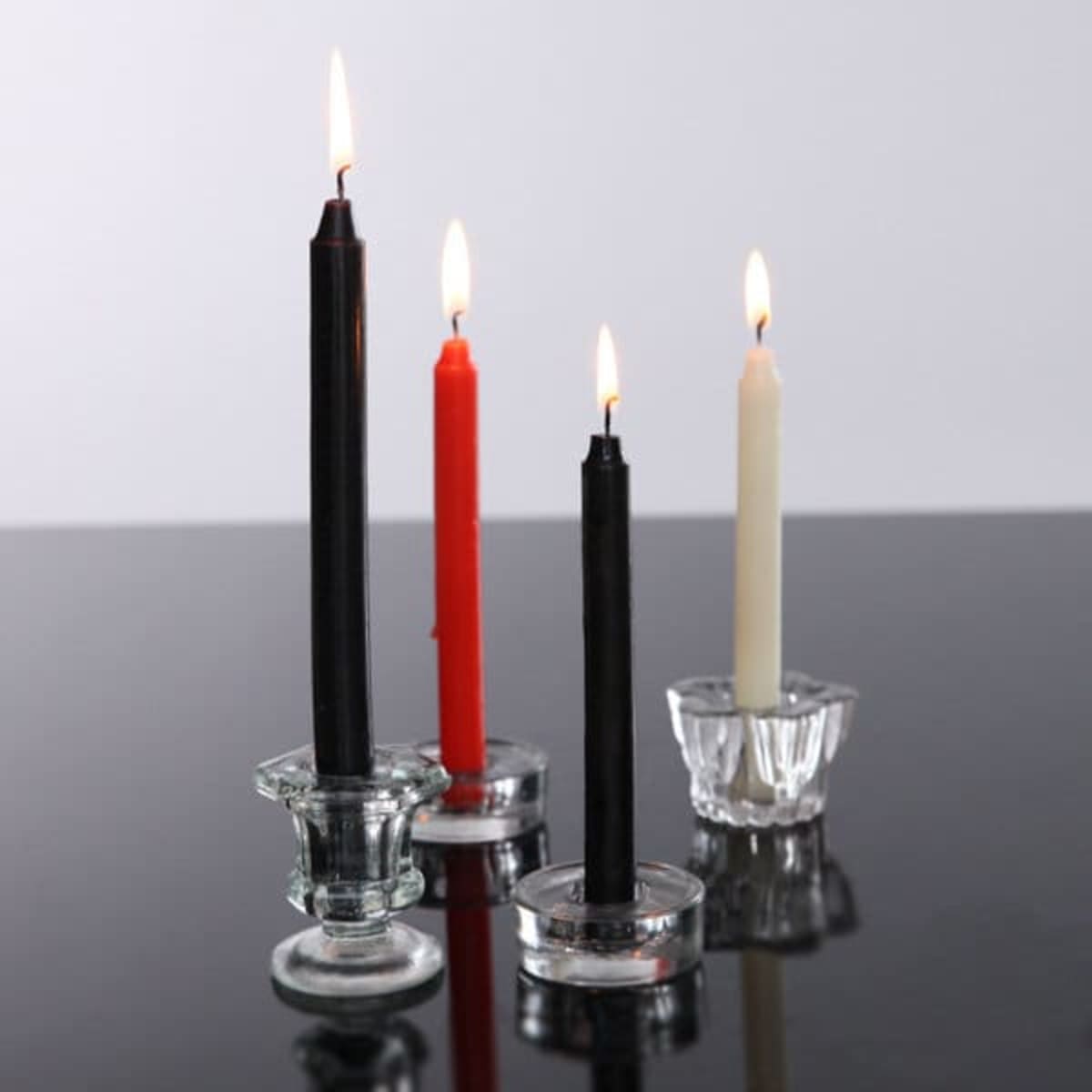 A set of four taper candles in black, red, and cream, displayed in clear glass candle holders, with flames lit.
