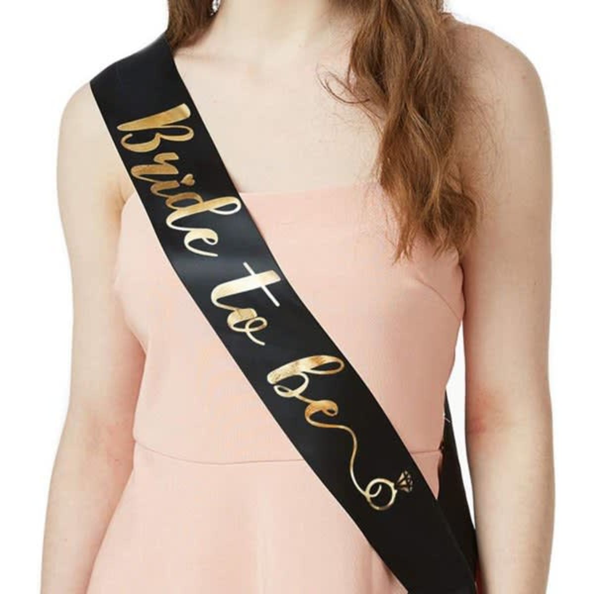 A black satin sash with gold text reading "Bride to be," worn over a pink dress.