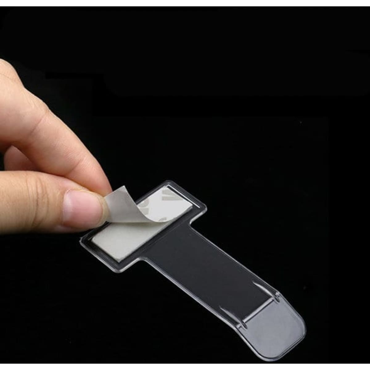 A transparent parking ticket holder with a peel-off adhesive backing, being held by a hand.