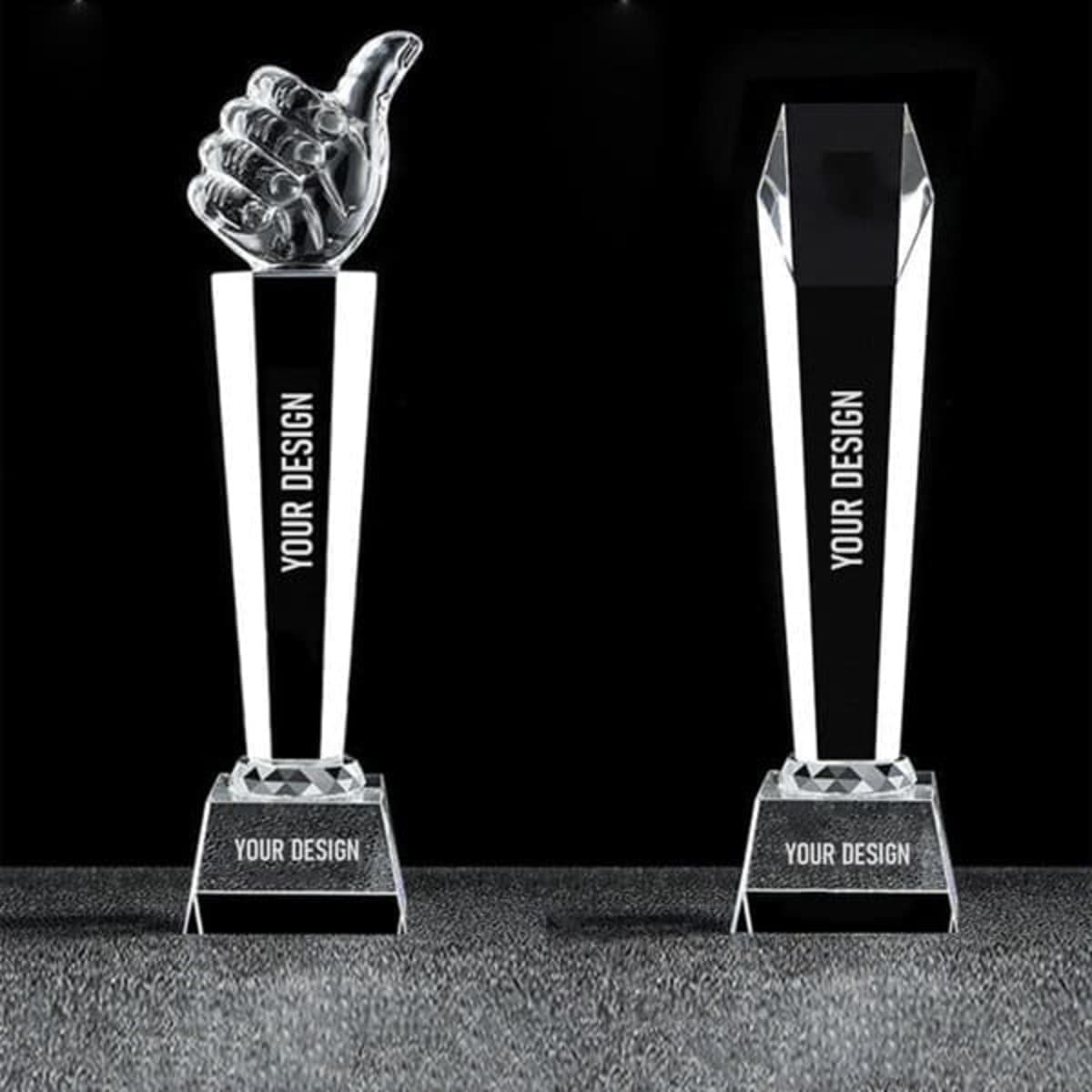 A crystal thumbs up trophy featuring a clear thumb design atop a rectangular base, with a black section for custom engraving.