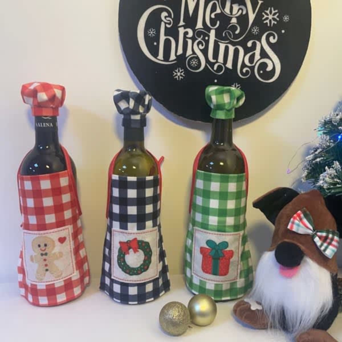 Three drink bottles in festive bottle aprons—red, black, and green check patterns with holiday-themed designs.