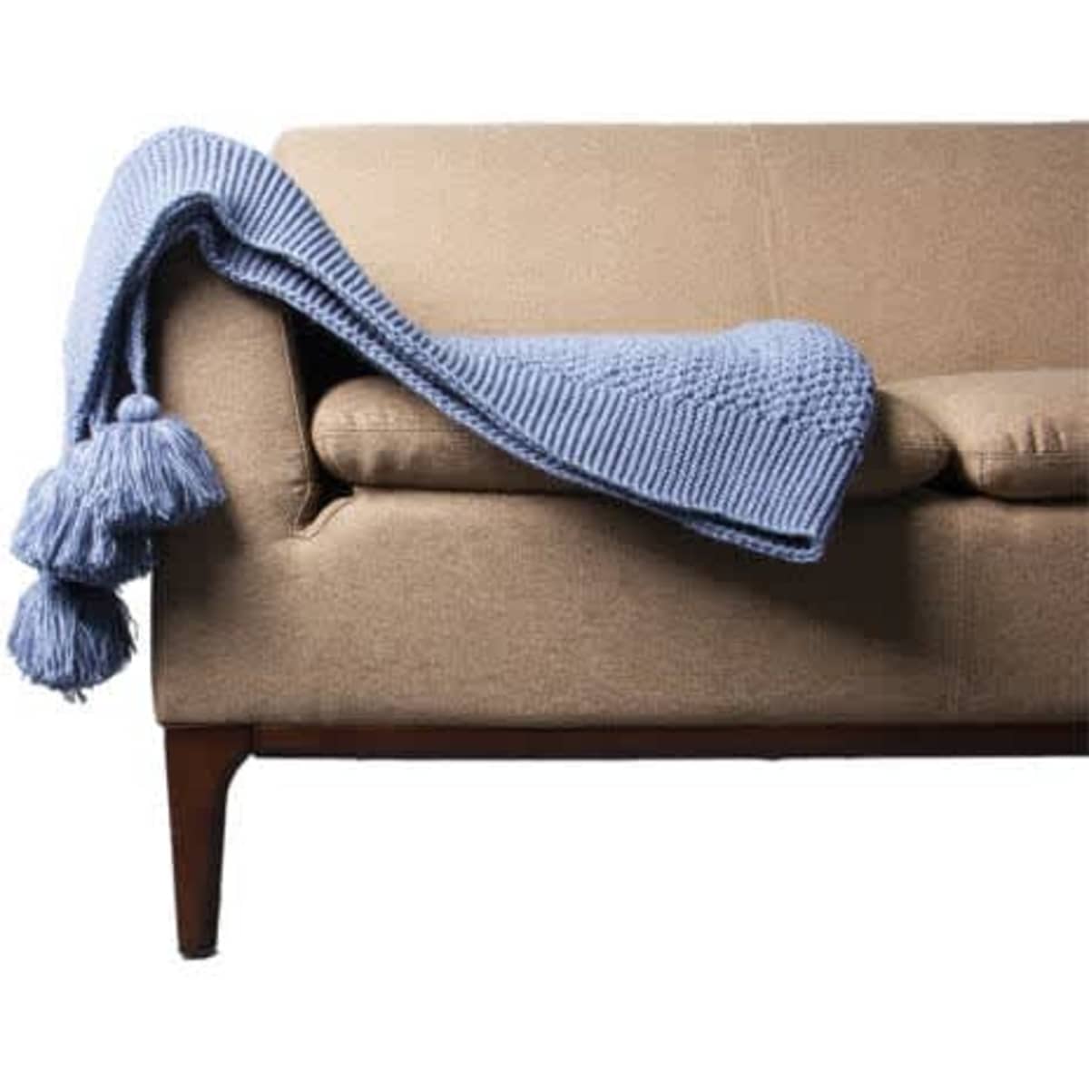 A blue knitted throw blanket with tassels draped over a beige sofa.