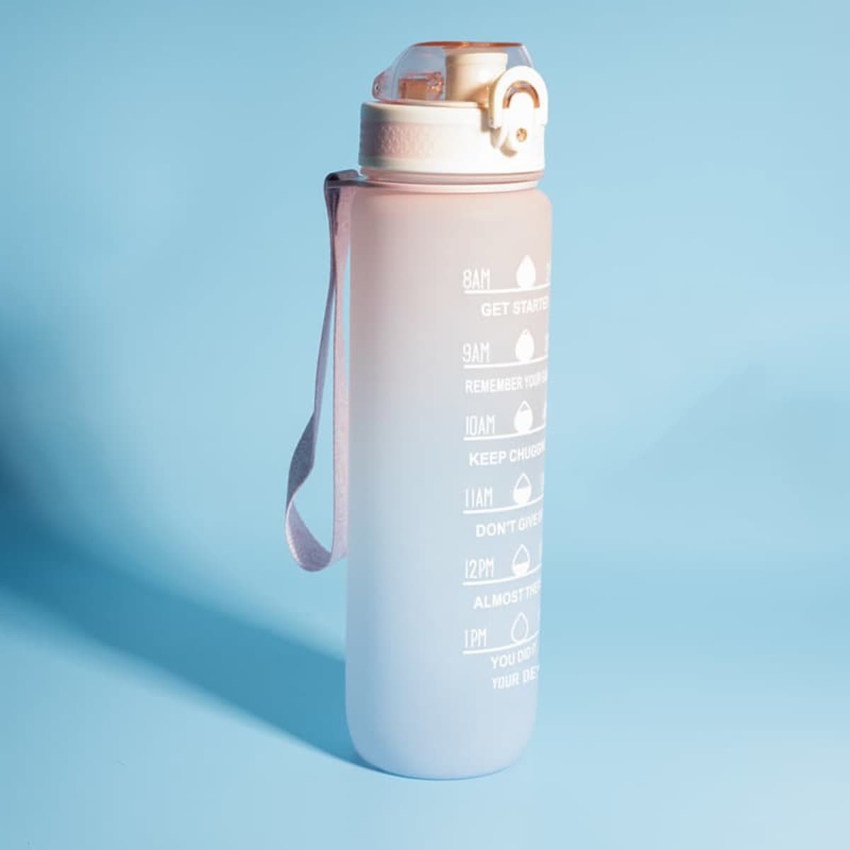 A drink bottle in a gradient pink and white design, featuring a time scale and a carrying strap.