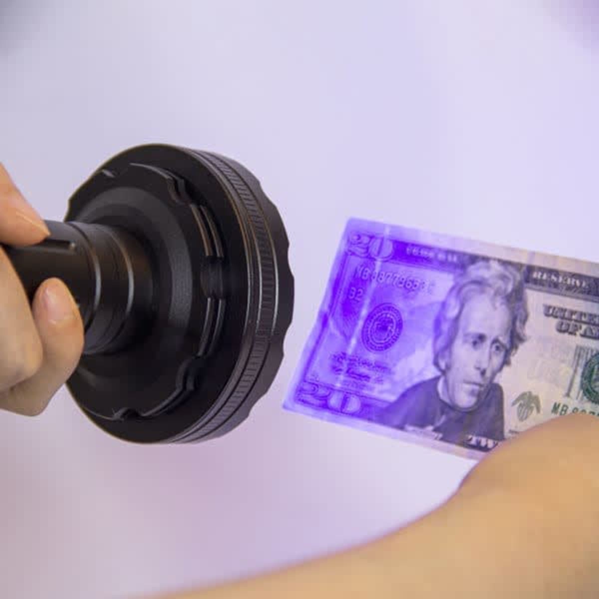 A UV LED flashlight in black is illuminating a banknote, highlighting its security features.