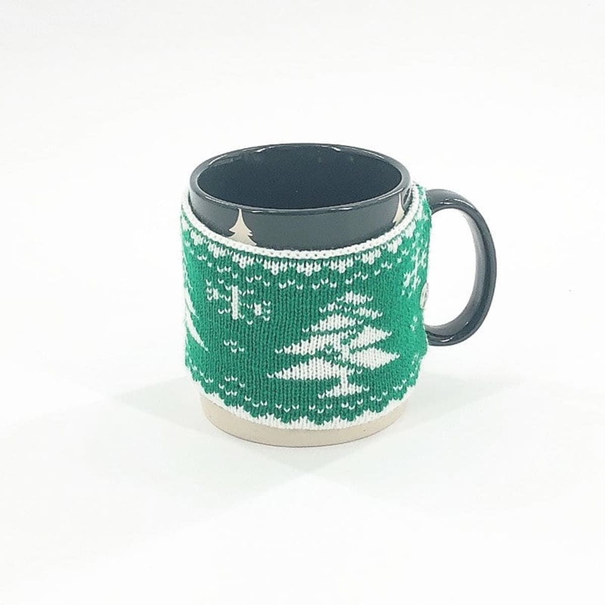A black coffee mug with a green knitted cup sleeve featuring a winter design. The sleeve is decorated with white patterns.
