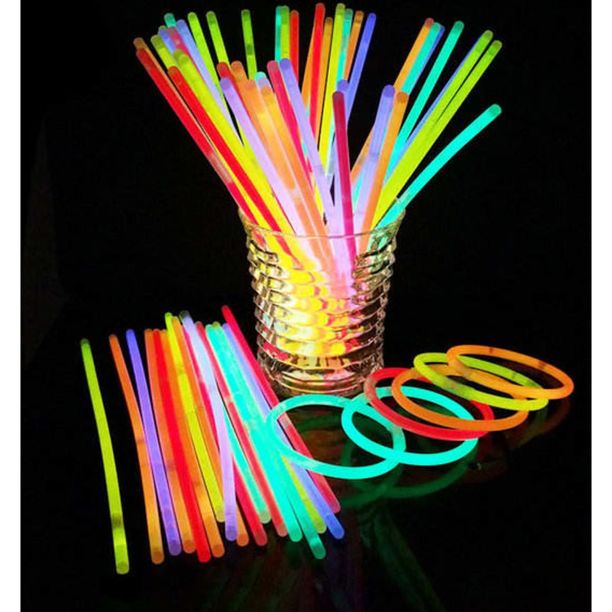 A collection of vibrant glow stick bracelets and sticks in assorted colours, arranged in a glass container on a dark surface.