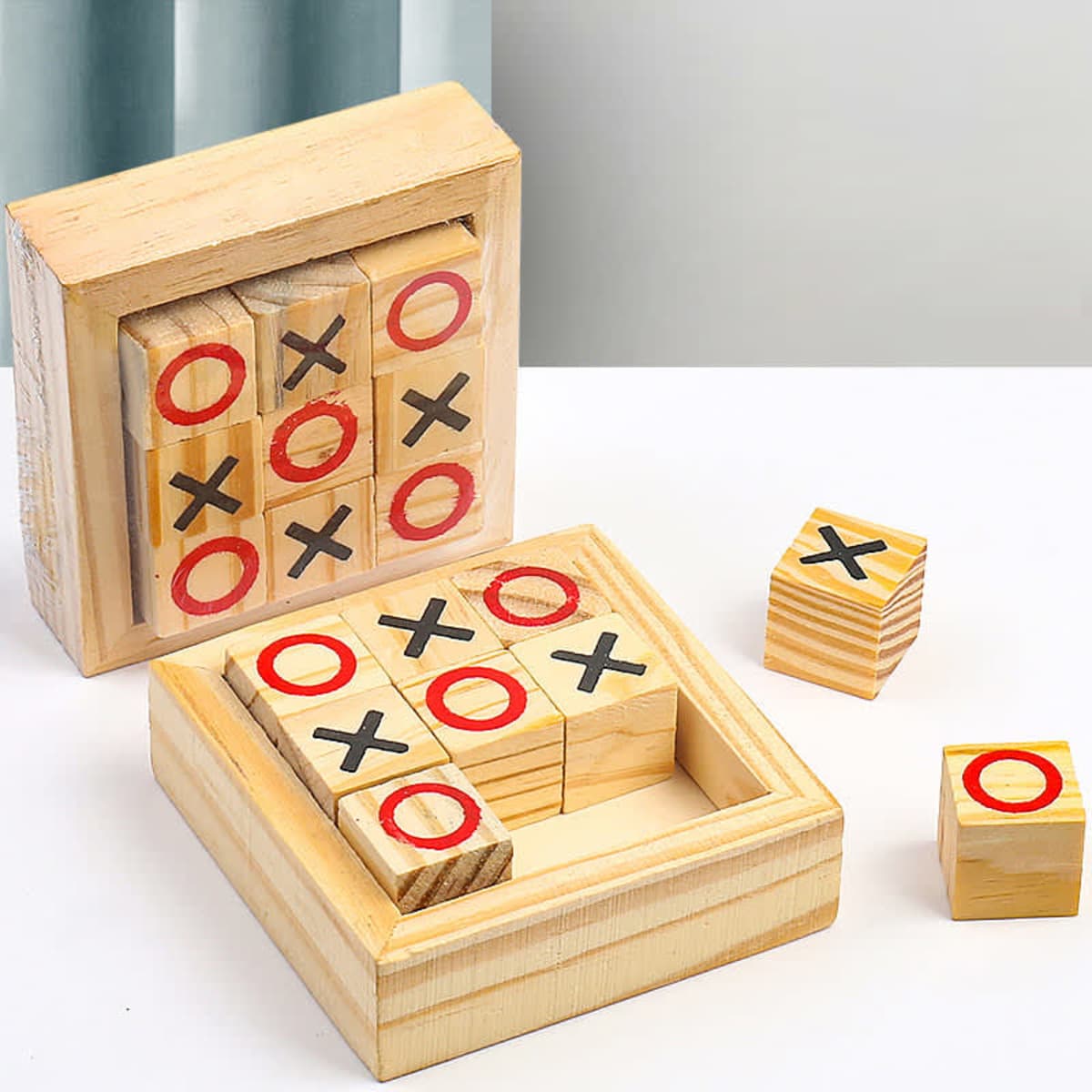 A wooden tic-tac-toe game with red and black markings on square blocks in a natural wood box.