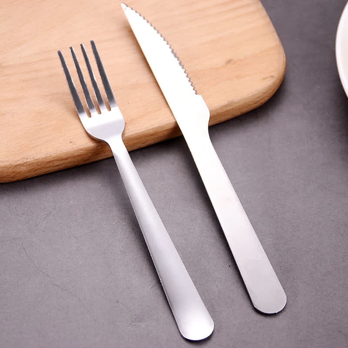 A stainless steel cutlery set featuring a fork and a knife, resting on a wooden surface.