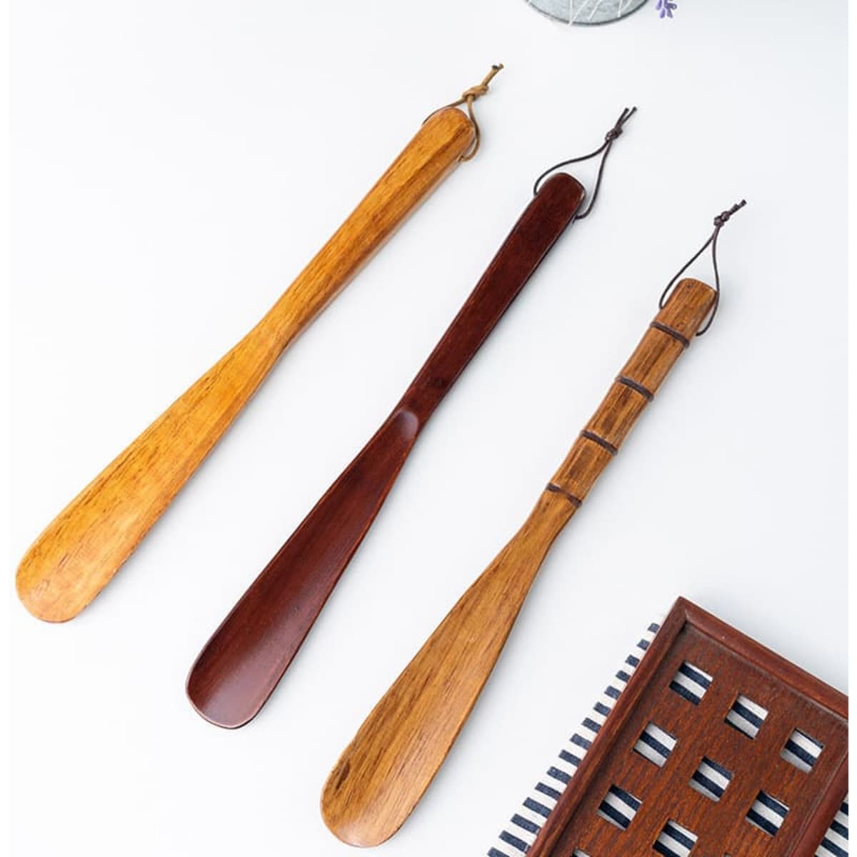A set of three custom wooden shoe horns in different wood shades, featuring varied designs and a leather loop.