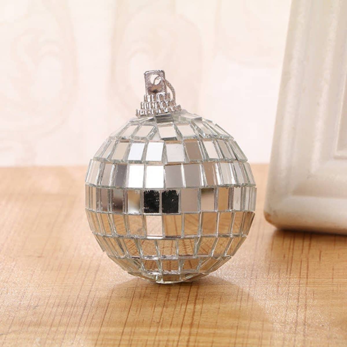 A mirrored Christmas ball ornament with a shiny, reflective surface sitting on a wooden table.