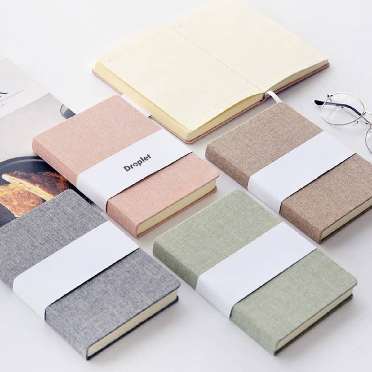 A collection of classic cloth bound notebooks in grey, pink, beige, and green, with a white band around them.