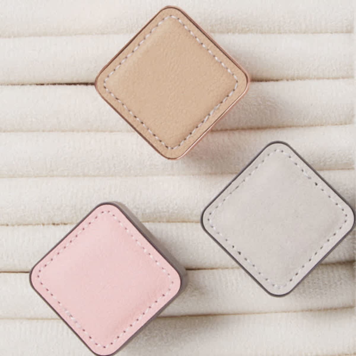 Three square air freshener clips in beige, pink, and grey, displayed on a textured white background.
