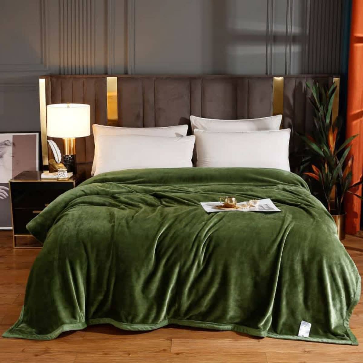 A plush, green flannel lap blanket is draped over a neatly made bed with pillows and bedside decor.