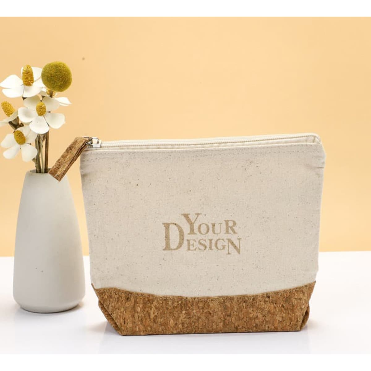 An eco-friendly zipper pouch featuring a cream canvas body and a cork base, positioned beside a small vase of flowers.