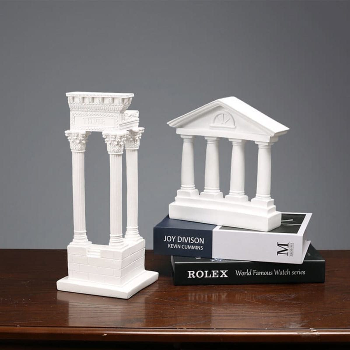 A pair of white resin 3D model ornaments resembling classical architecture, displayed on a stack of books.