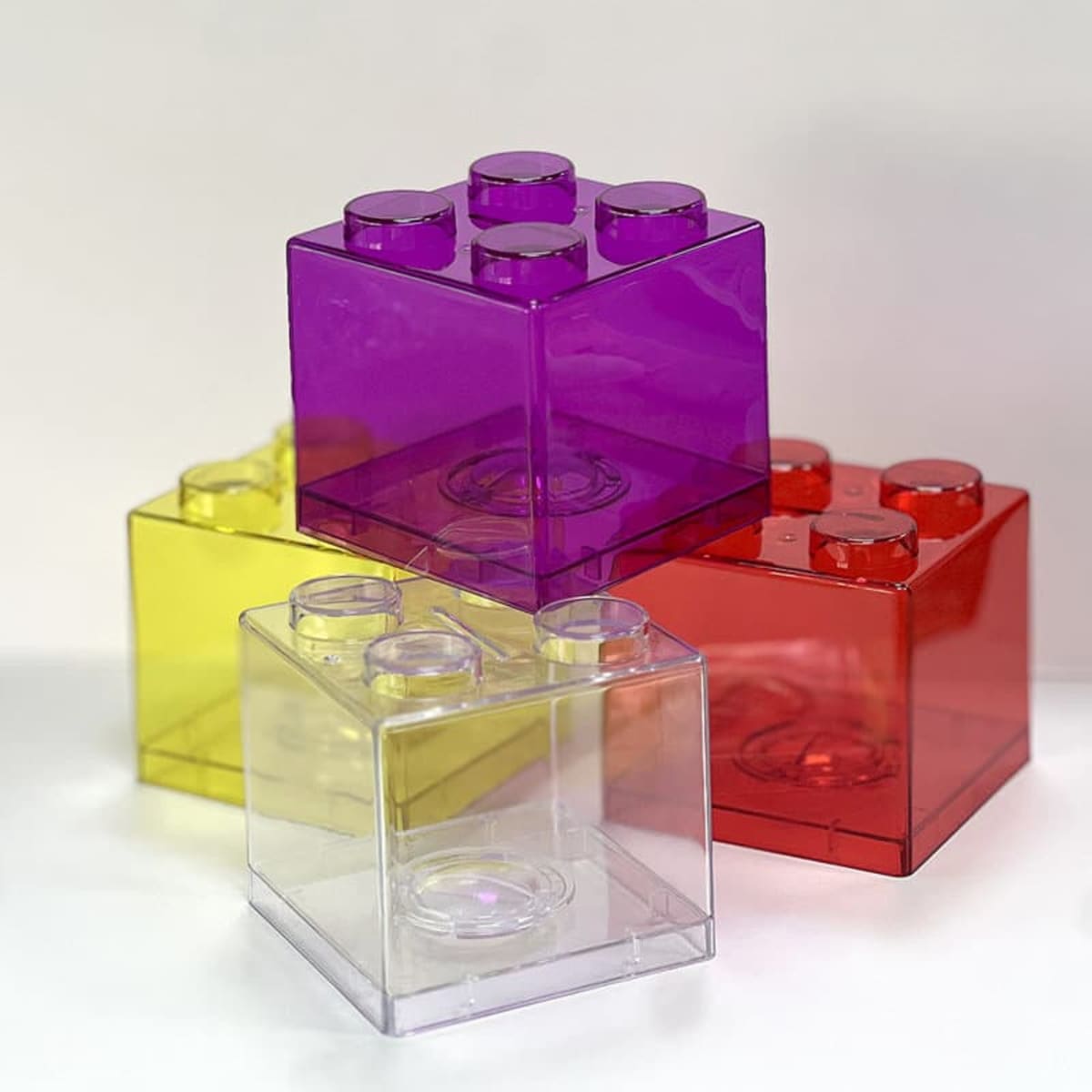 A set of colourful building block piggy banks in purple, yellow, red, and clear transparent plastic.