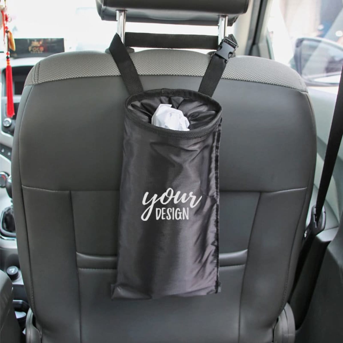 A black car seat back garbage bag hangs from the headrest, featuring a drawstring closure and a simple logo.