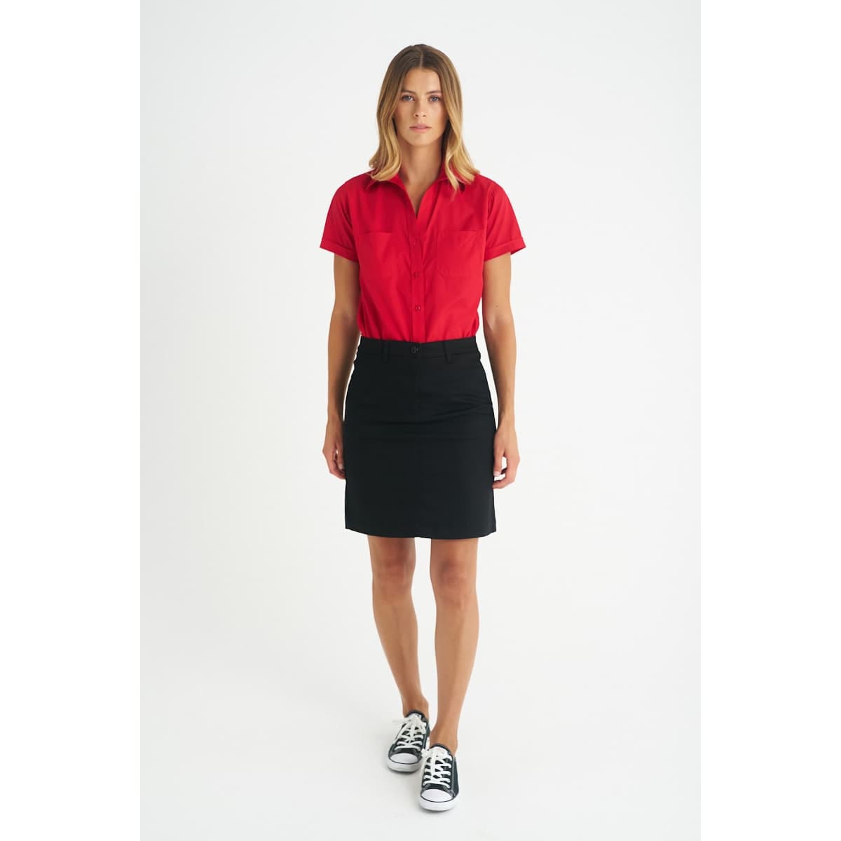 A model wearing a red shirt and a black chino skirt, with a pair of black and white sneakers.